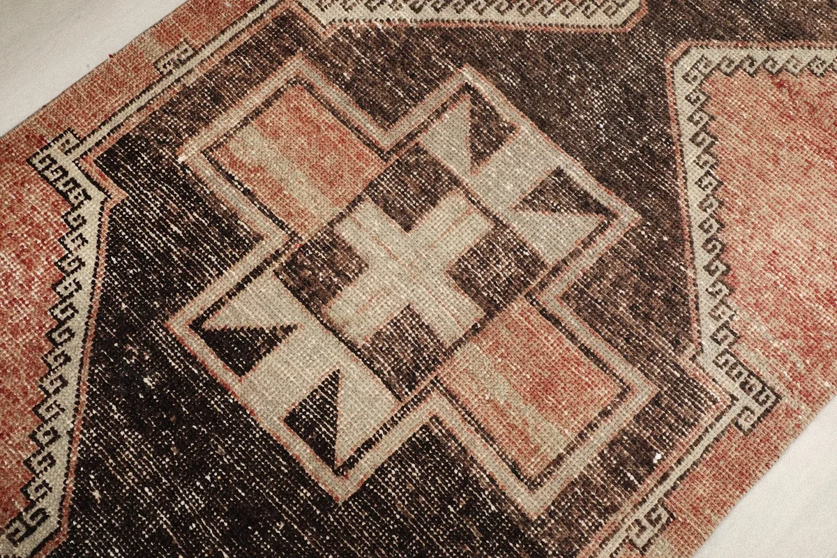 Close-up of a central geometric motif in charcoal and beige, showcasing the hand-knotted texture and color variation.