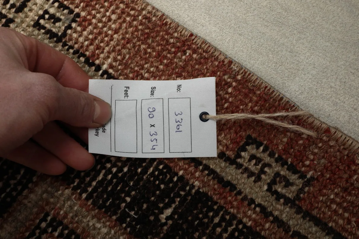 Hand holding a tag showing the rug's dimensions (90 x 354 cm), confirming its authenticity and size.