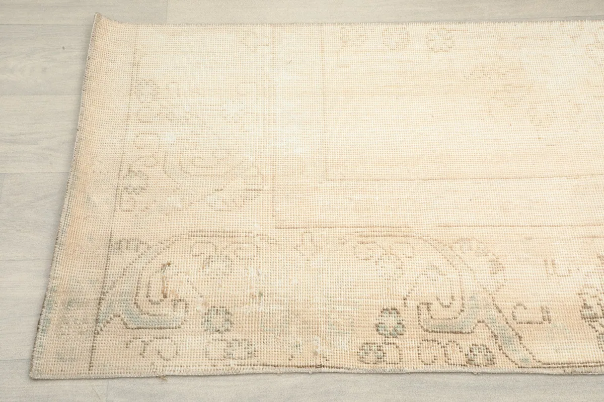 Detailed view of the rug's edge and subtle tan patterns against the beige field