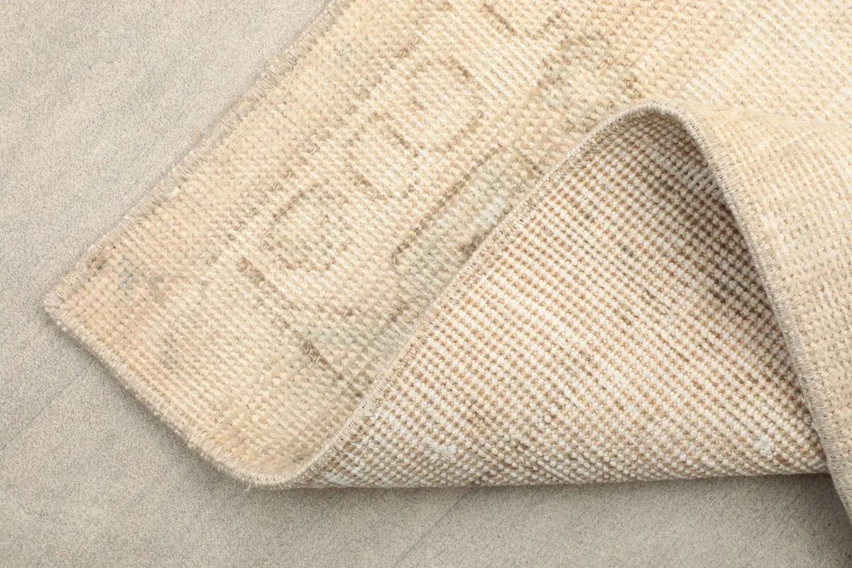 View of the underside (cotton foundation) and a corner of the beige hand-knotted rug