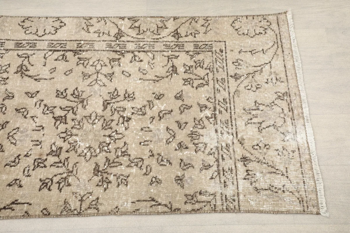 Close-up detail of the tan rug's border with intricate brown floral patterns
