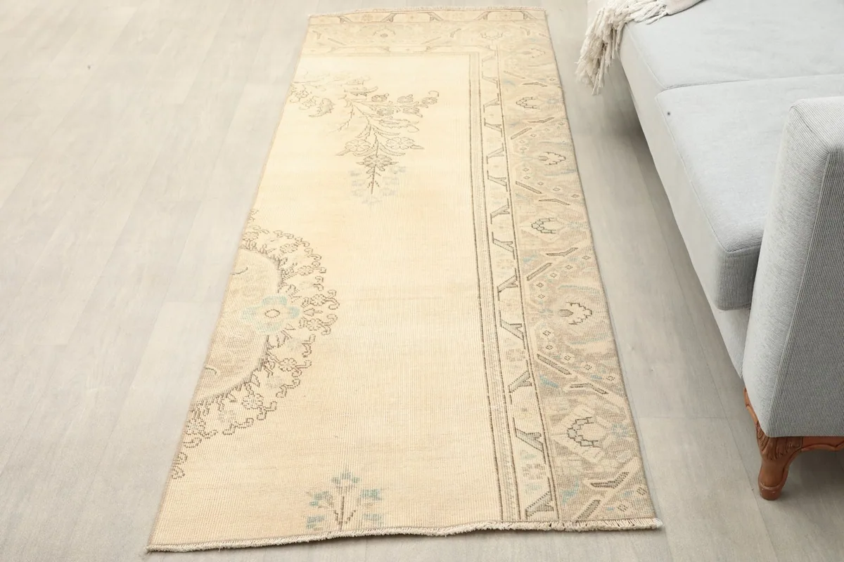 Overhead view of the cream runner rug laid on a light floor next to a gray sofa.