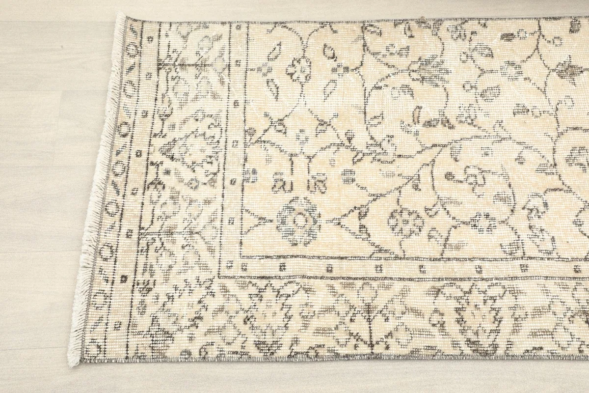 Detailed view of the rug's edge and corner, illustrating the intricate charcoal motifs against the beige