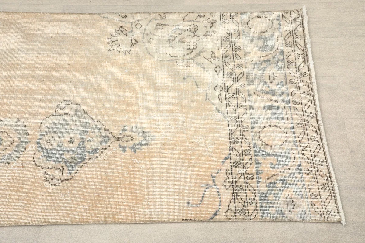 Close-up detail of the rug's beige field, faded blue floral motifs, and geometric border.