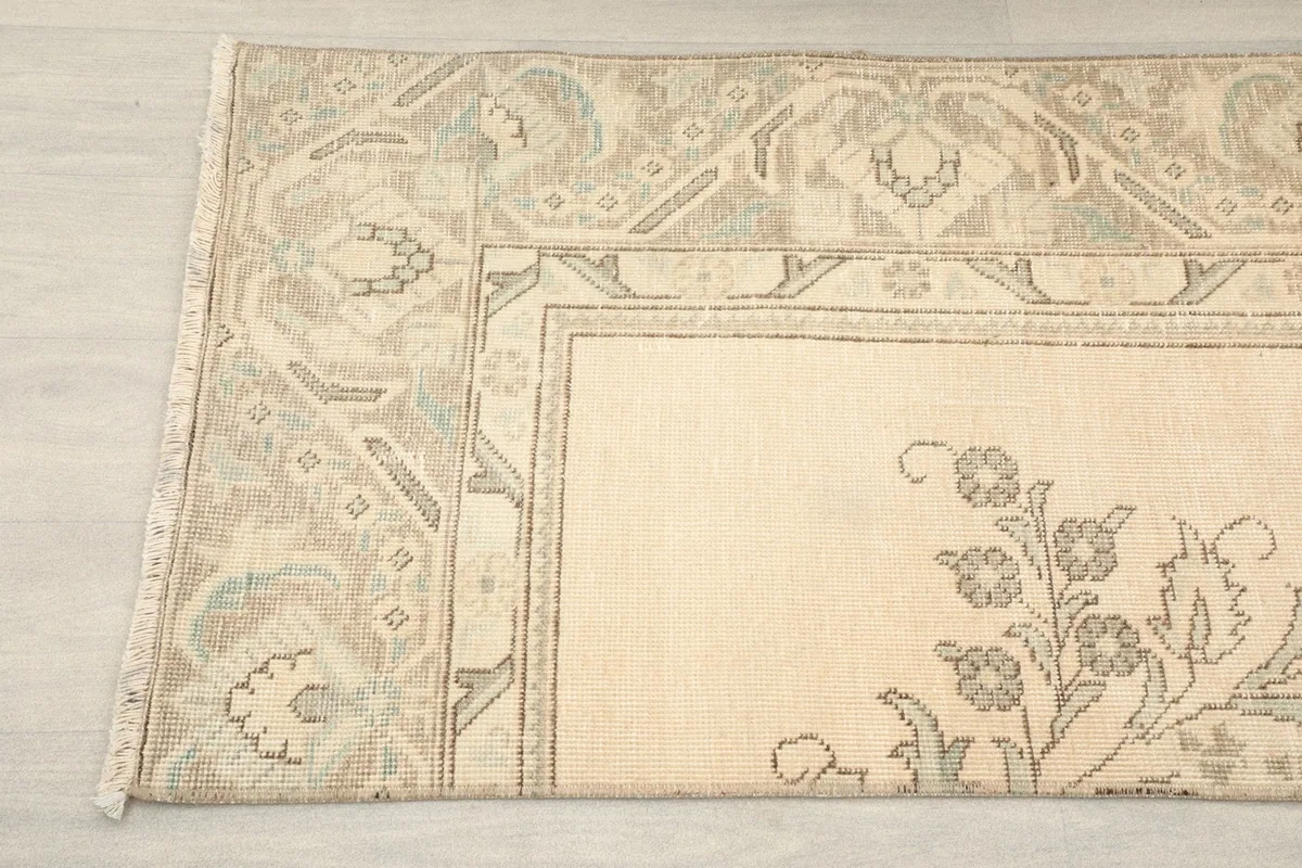 Detail shot of the rug's end, highlighting the subtle floral and geometric motifs in cream and gray.