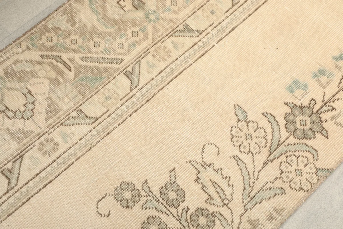 Close-up of the rug's surface, showing the blend of cream, gray, and olive tones in the floral design.