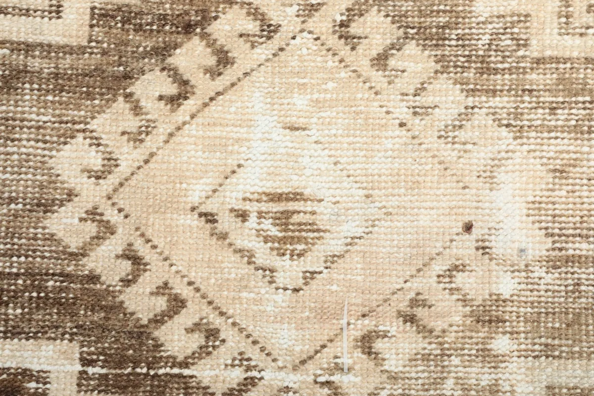 Extreme close-up showing the hand-knotted wool pile and the subtle variations in the beige and brown colors.
