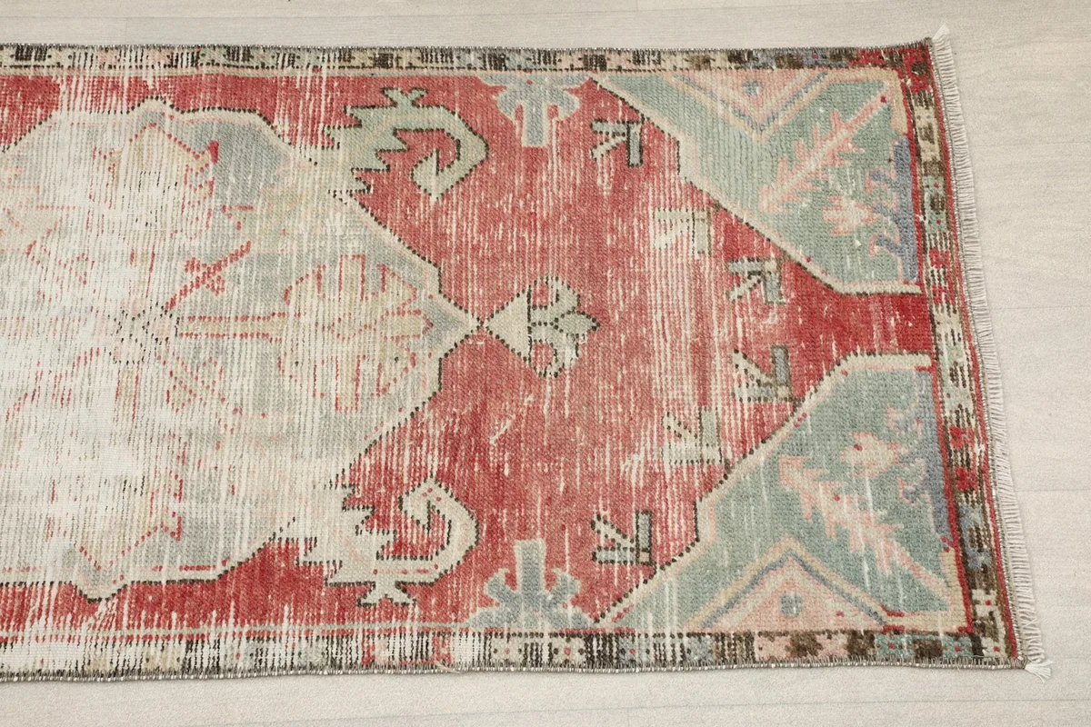Close-up of one end of the runner rug, showing the geometric pattern and distressed red and blue tones.