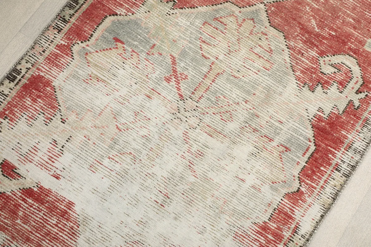 Close-up of the faded ivory and red pile, highlighting the intricate hand-knotted texture and wear.