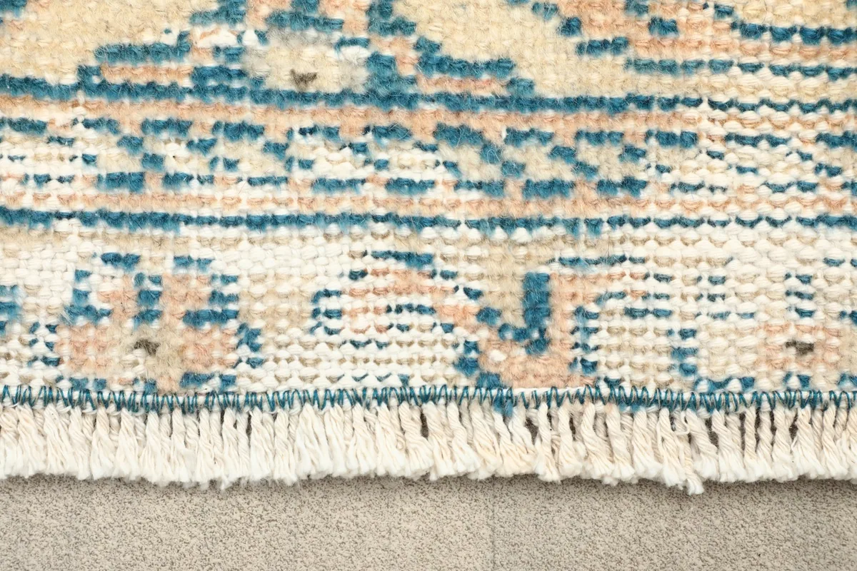 Close-up view of the rug's fringe and a section of the border pattern in blue and beige.