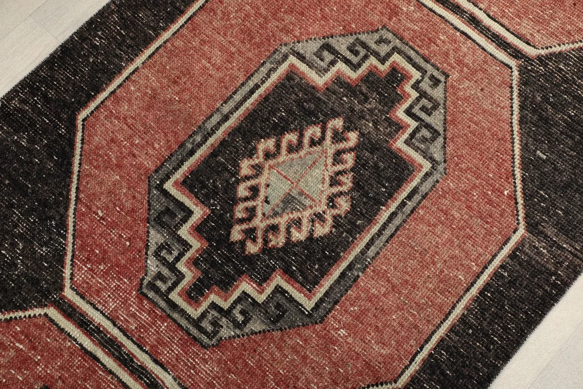 Close view of a central medallion, showing the faded rust, black, and ivory wool pile.
