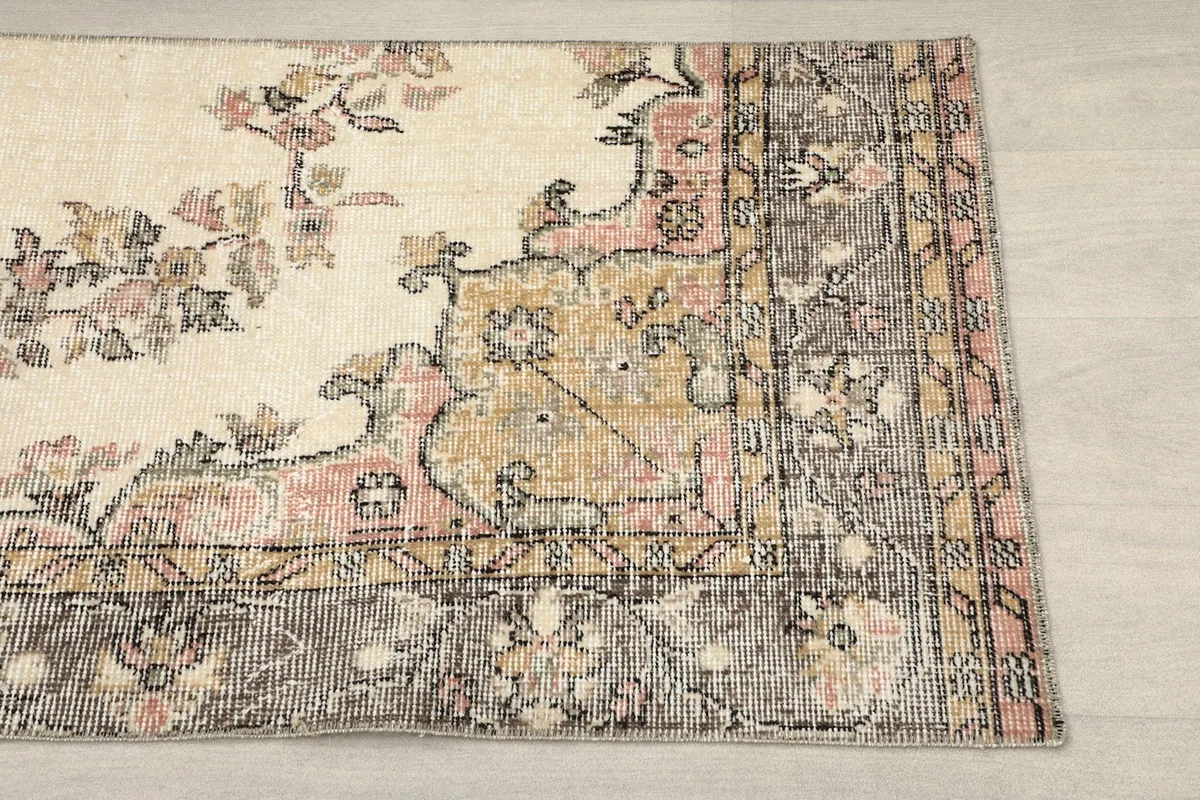 Close-up of the rug's corner, showing the muted rose and gold floral patterns against the ivory field and gray border.