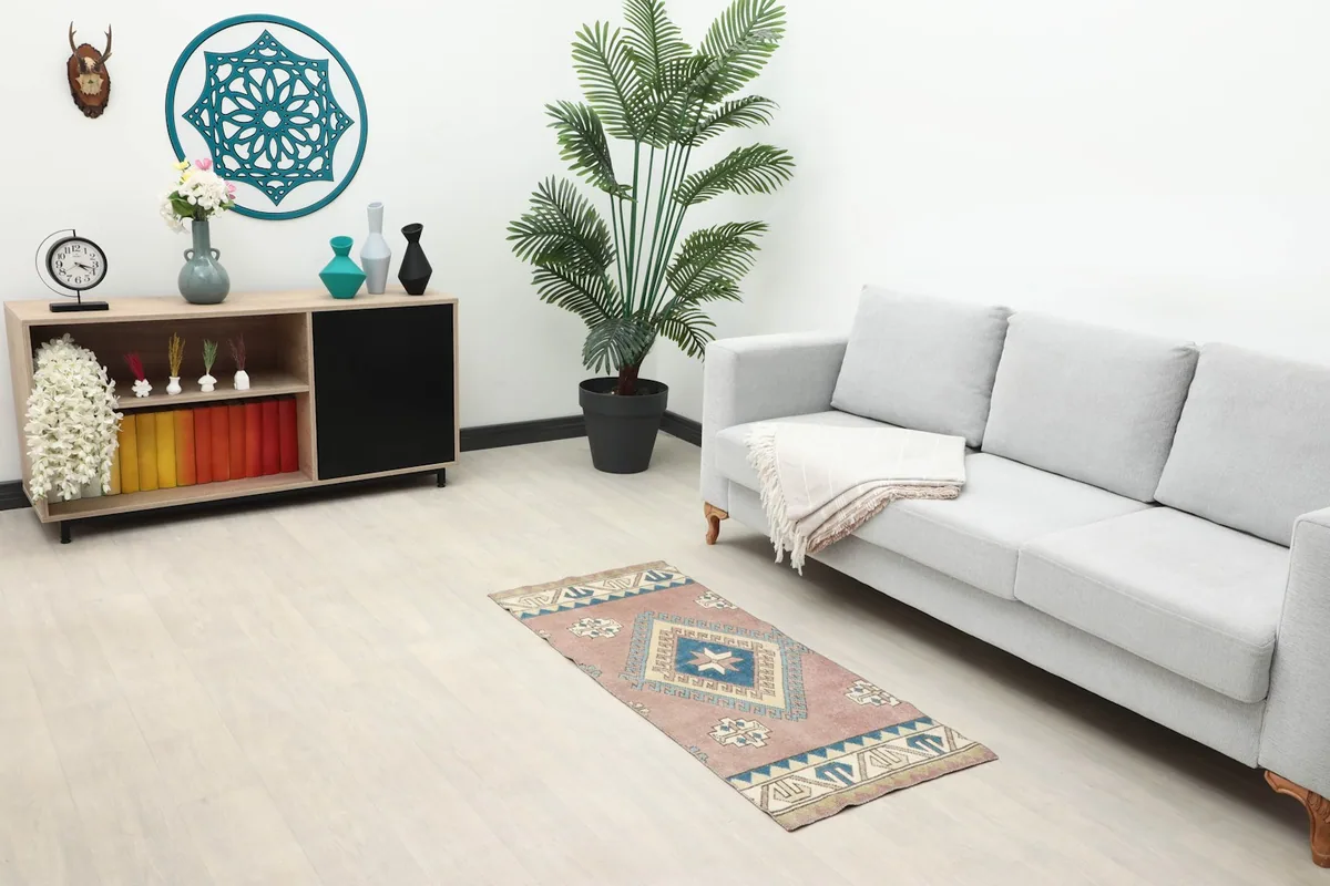 The rose and blue vintage rug displayed in a modern living room setting, next to a light gray sofa.