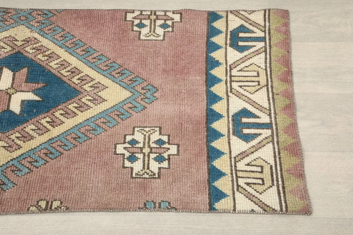 Close-up of the upper right section of the rug, highlighting the geometric patterns and border in rose, blue, and beige.