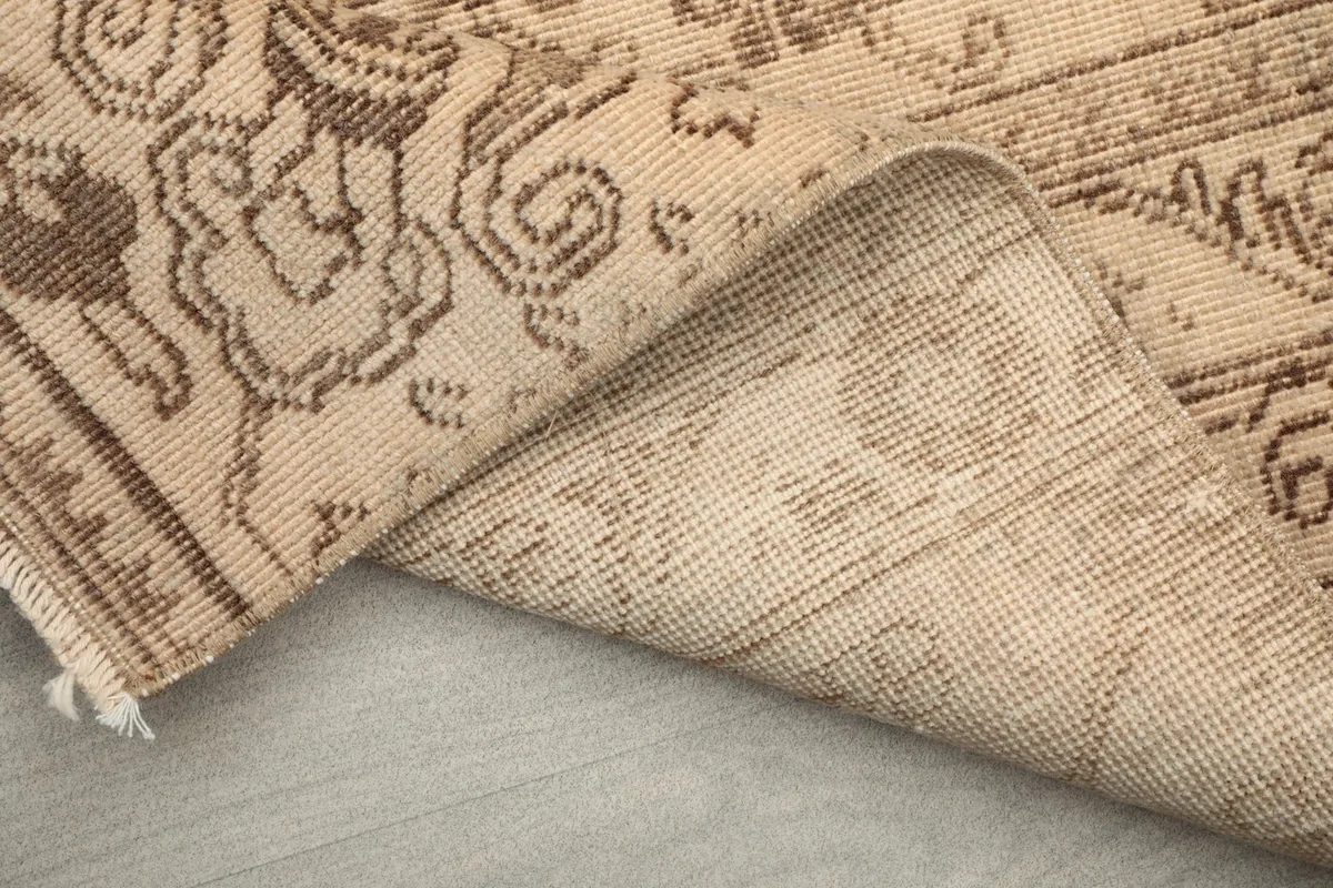 Underside of the rug visible as it is folded, showing the hand-knotted cotton foundation