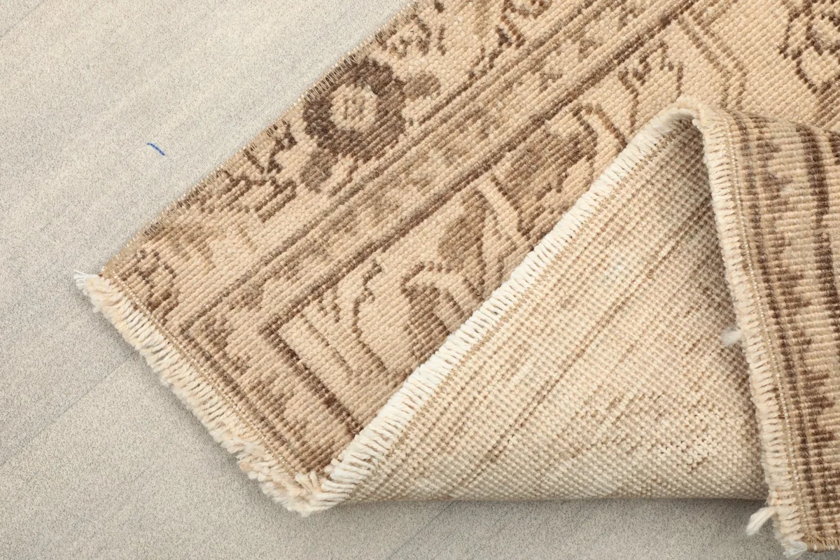 Corner of the rug folded back, revealing the cotton foundation and fringe