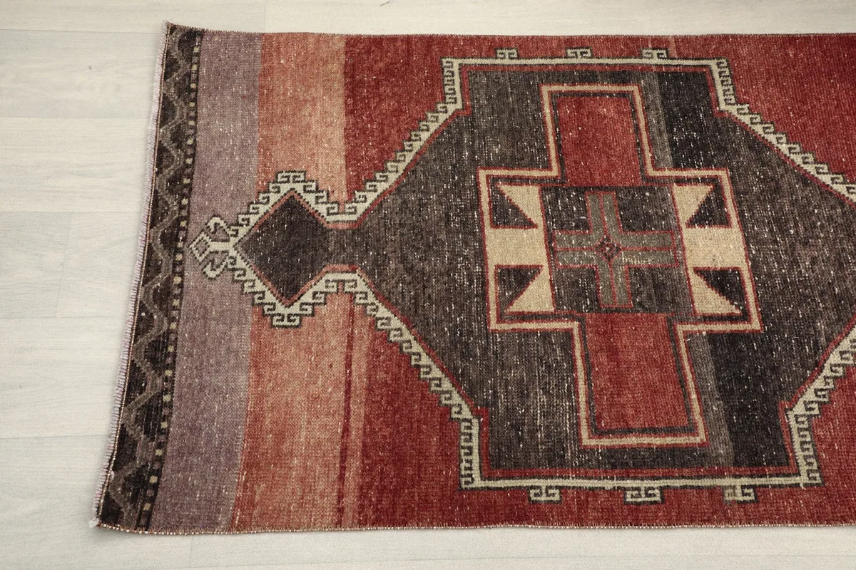 Detail of the runner rug's end, showing the charcoal and red patterns and subtle color variations