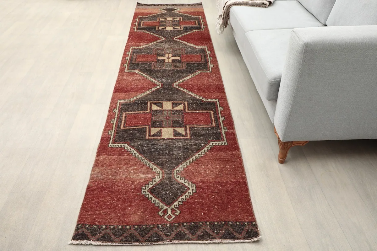 Vintage Anatolian runner rug with red and charcoal patterns placed in a modern living space next to a sofa