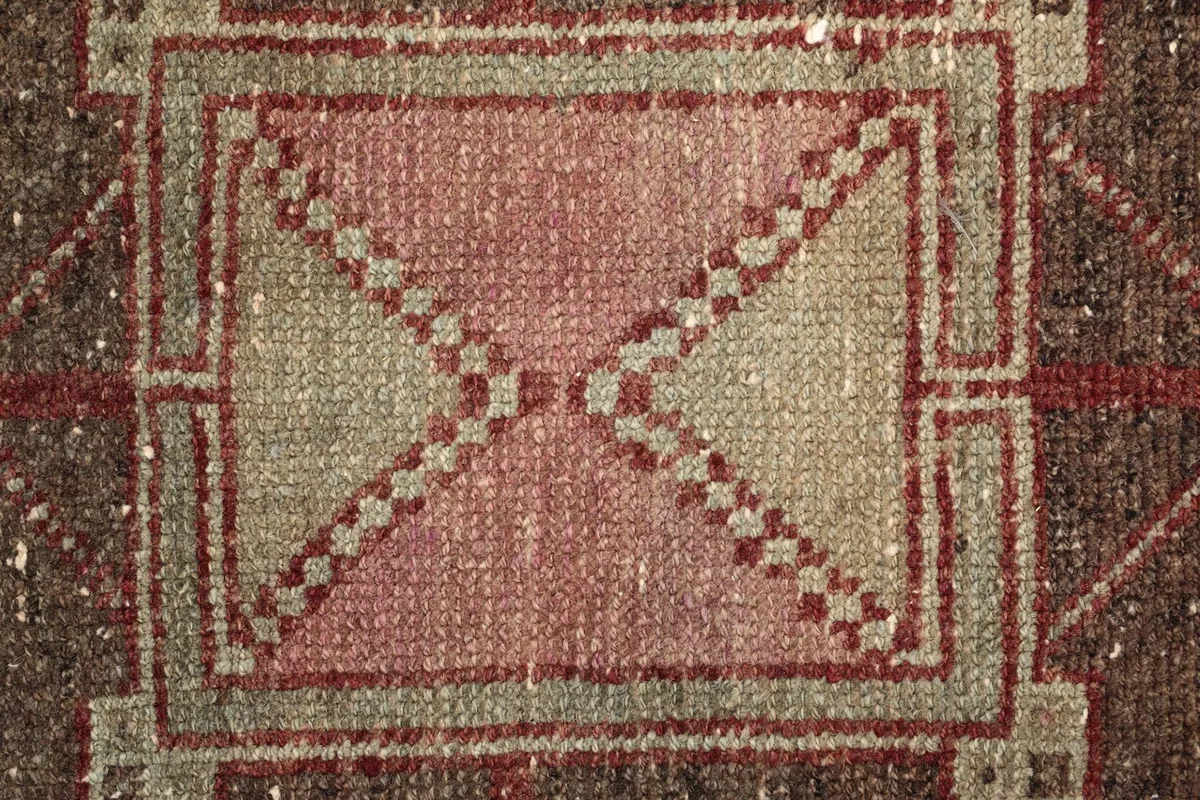 Close-up detail of a geometric motif within a medallion, showing red, beige, and pink tones.