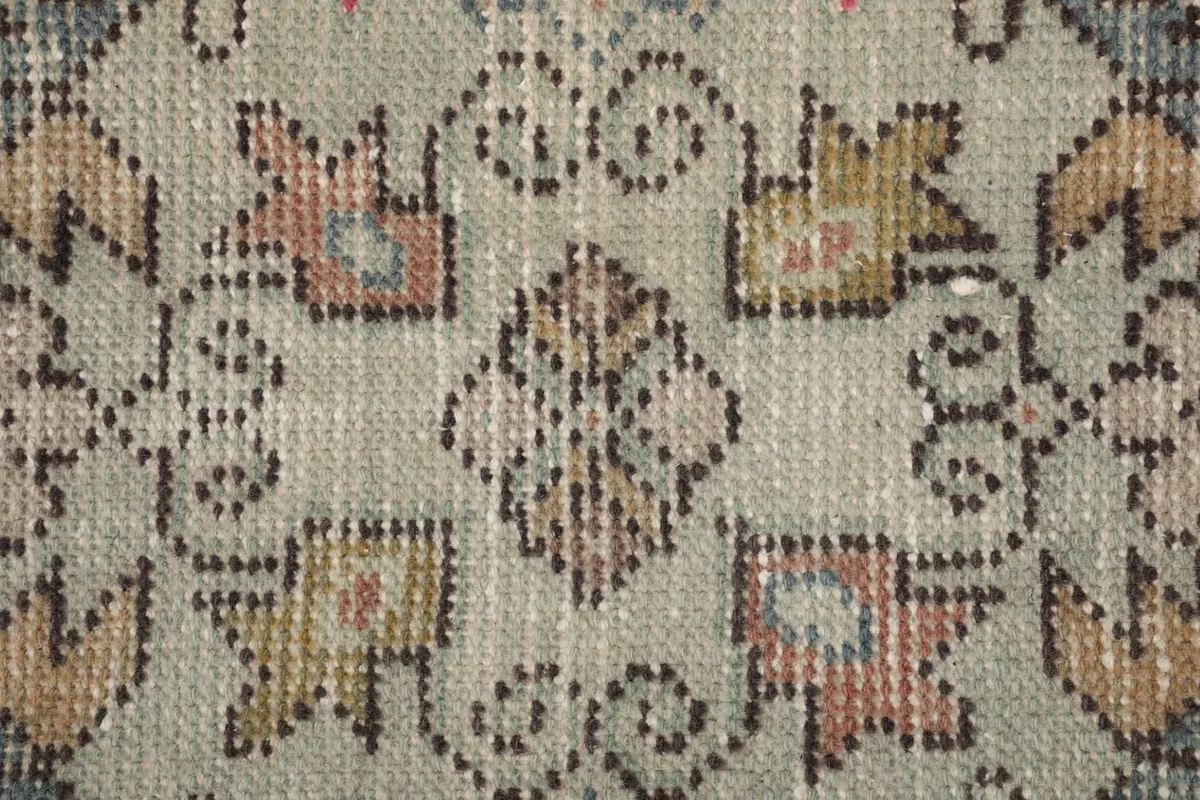 Extreme close-up of the rug's low wool pile, showing the hand-knotted texture and faded colors.