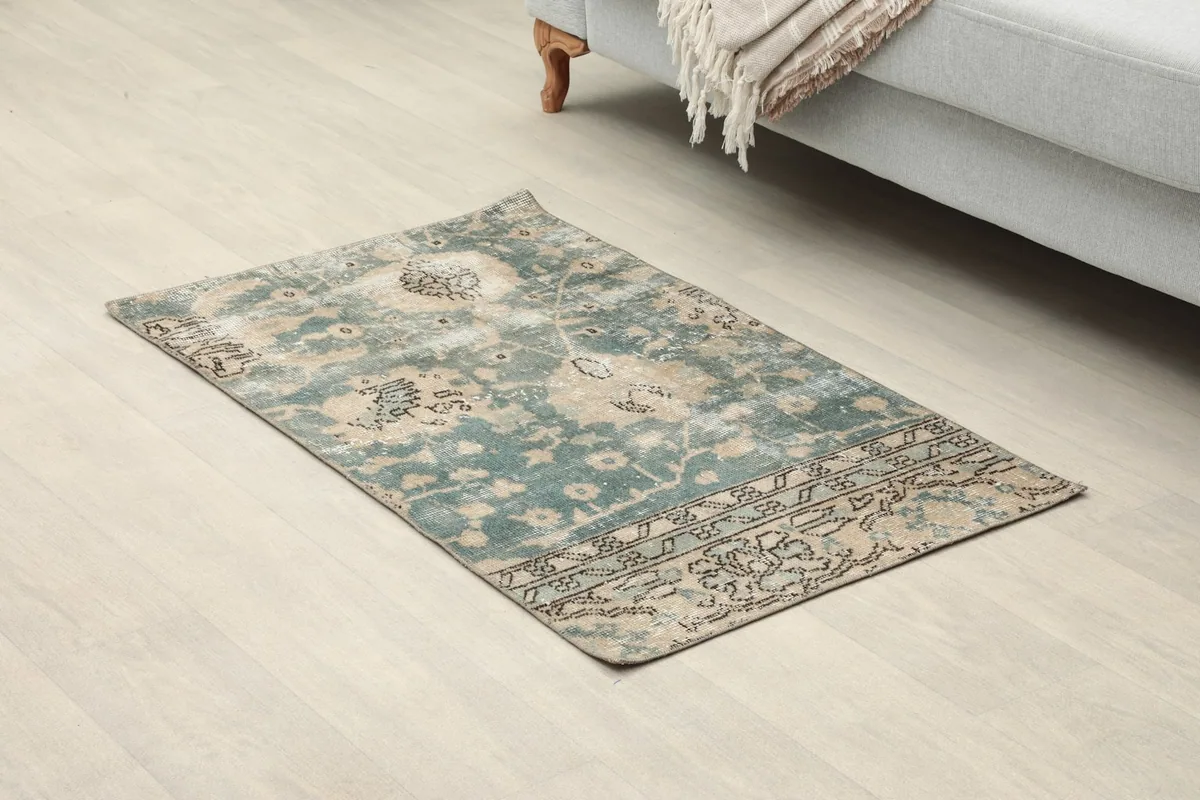 Angled view of the green and tan vintage rug on a light floor, showing its full design