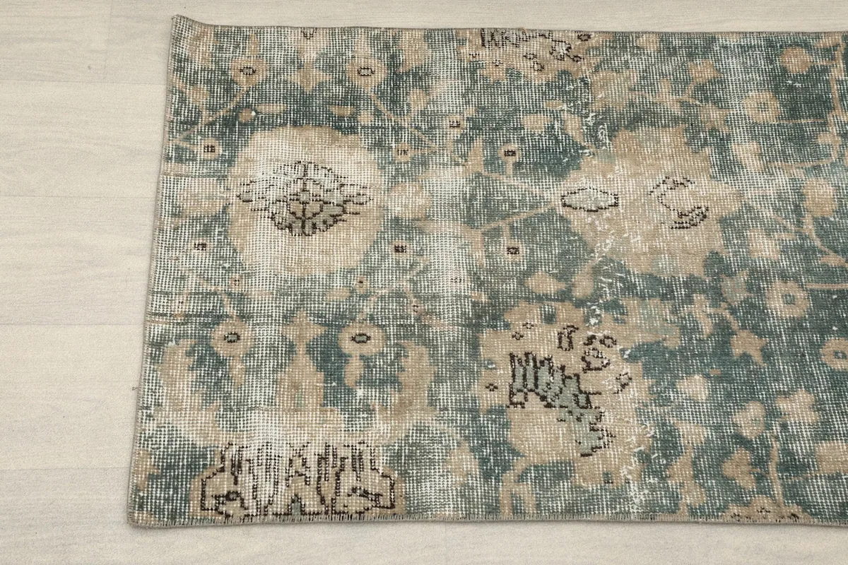 Detail view of the corner of the rug, showing faded green and tan patterns