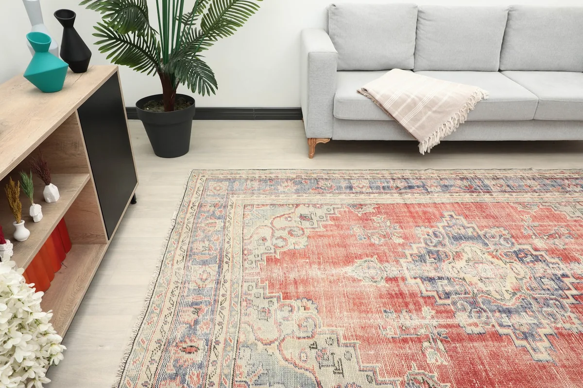 Angle view of the rug in a room, highlighting the red field and navy border next to a sofa.