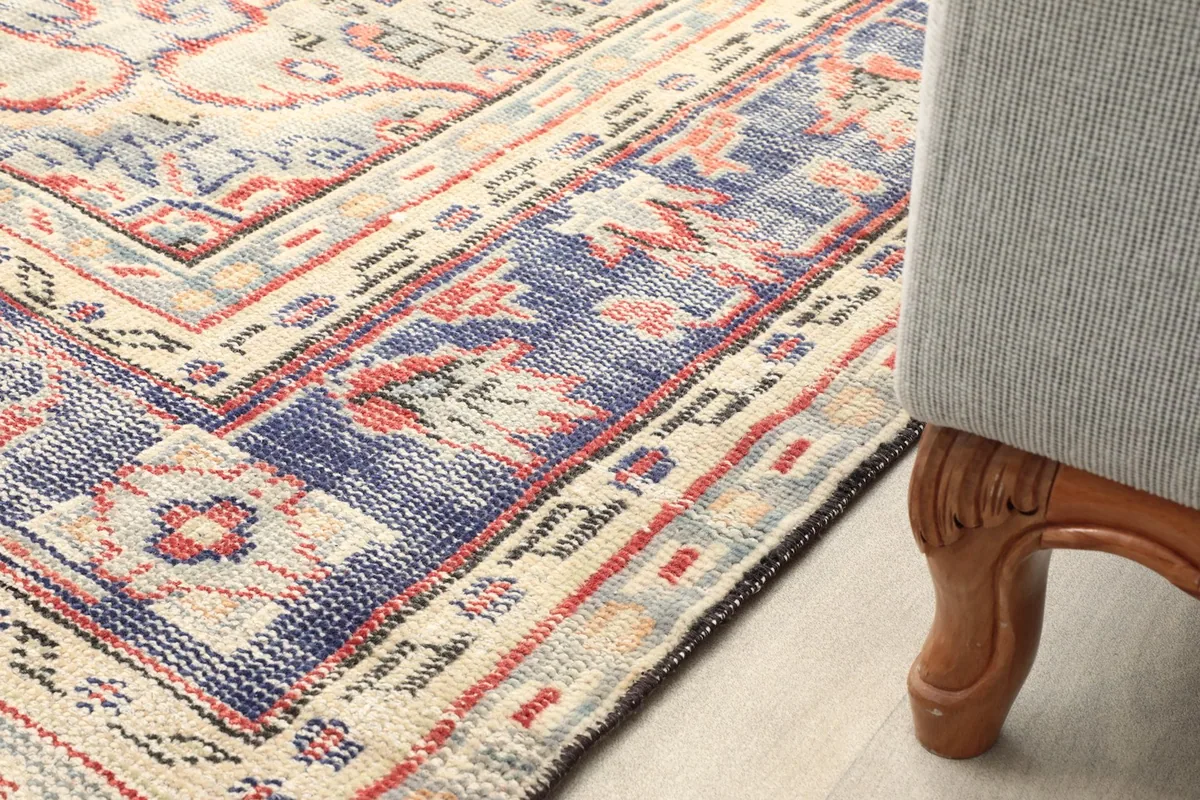Close-up of the rug's border next to a furniture leg, showcasing the colors and wear.