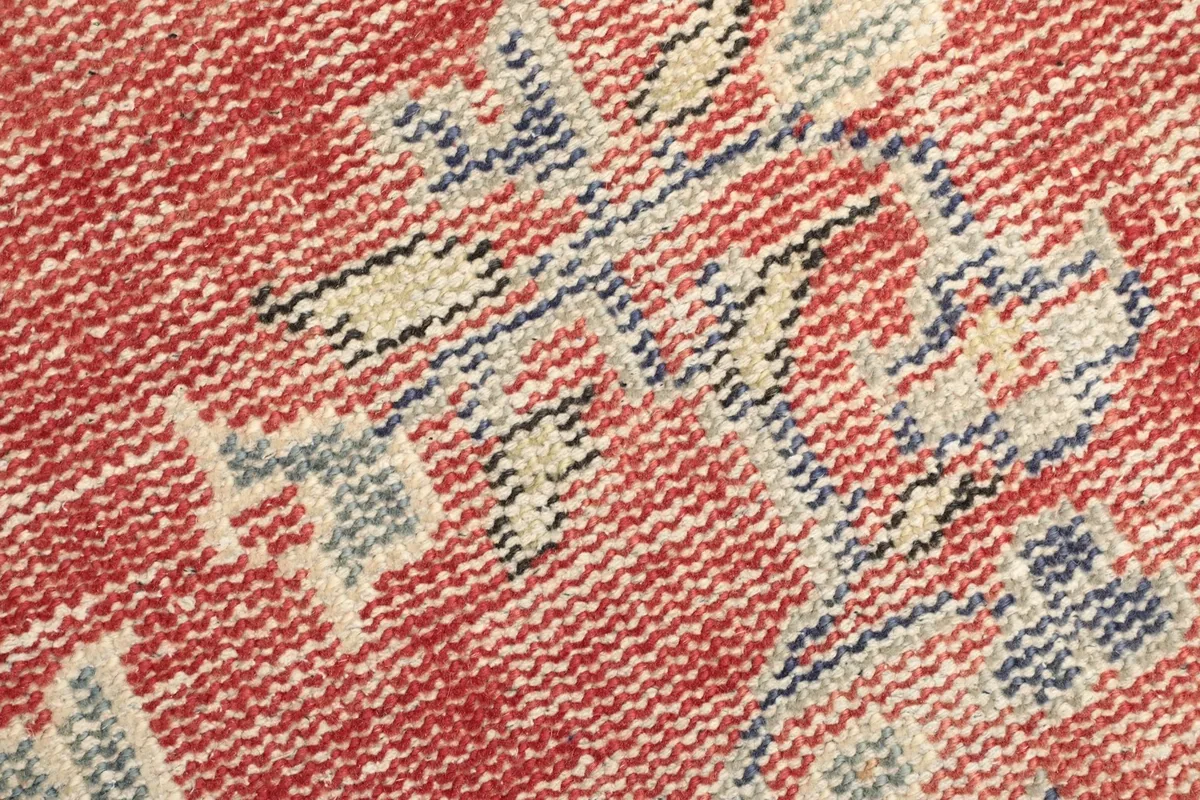 Detailed view of the low wool pile texture and the hand-knotted weave in red and blue tones.