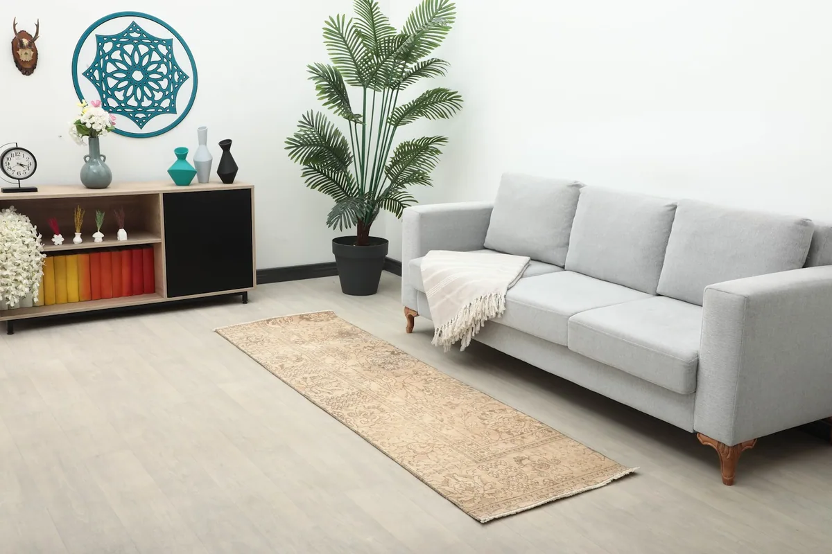 Long view of the beige runner rug stretching across a room with a sofa, cabinet, and plant.