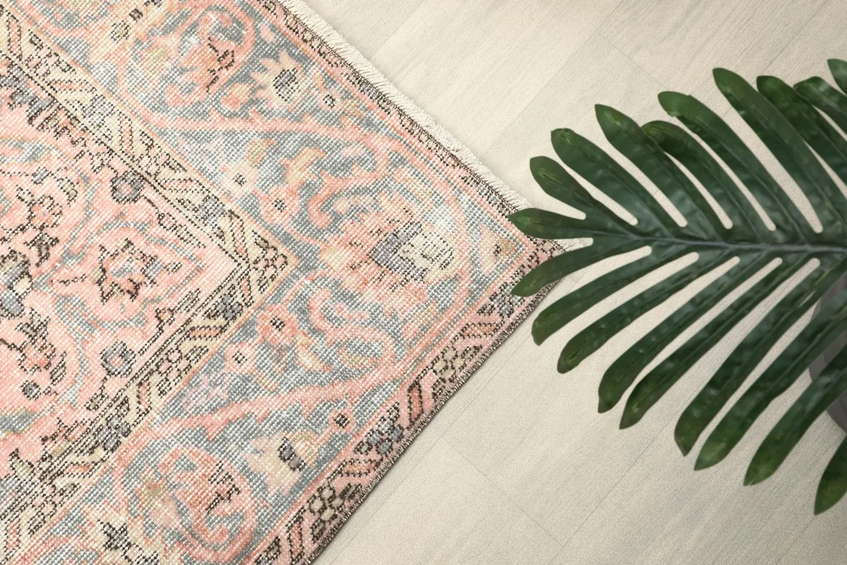 Corner detail of the rug with a plant leaf, showcasing the rose and gray palette