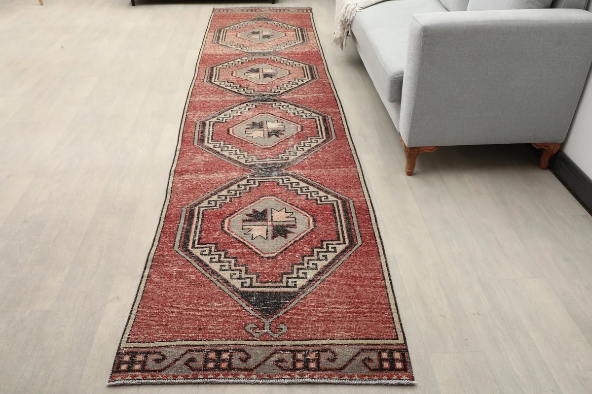Vintage rust runner rug extending from a light gray sofa in a room setting, showing its length.