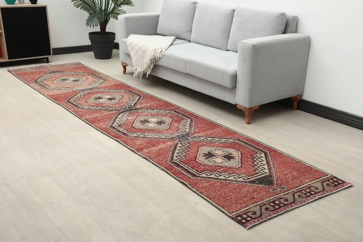 Angled view of the rust runner rug next to a gray sofa, showcasing its texture and colors in a home setting.