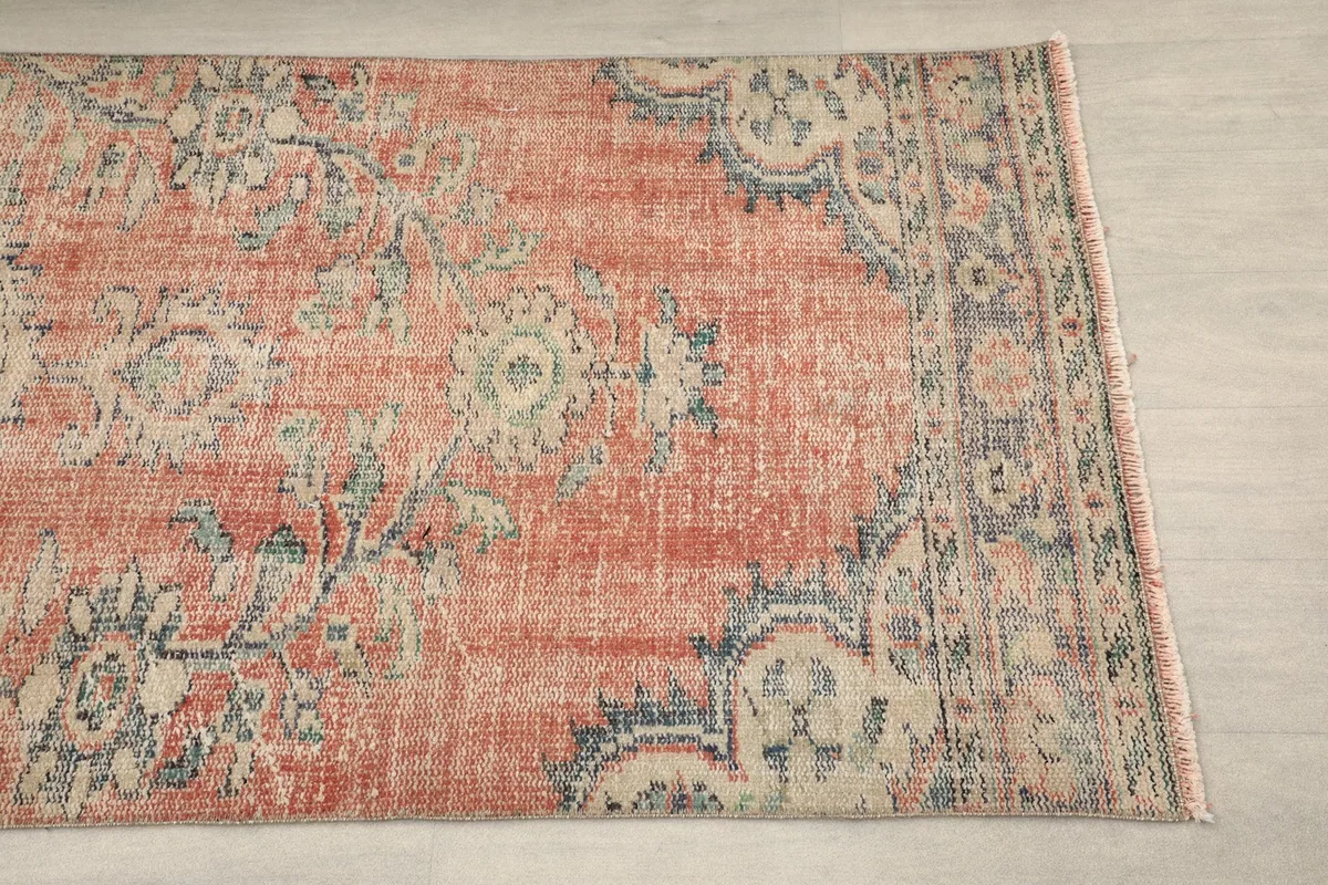 Close-up view of the rug's border and corner, showing faded rust and blue tones
