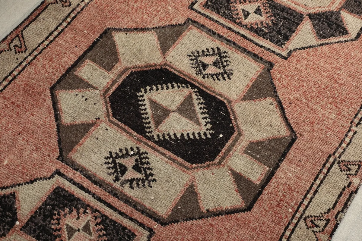 Detailed view of a black and beige geometric medallion within the rose field of the rug