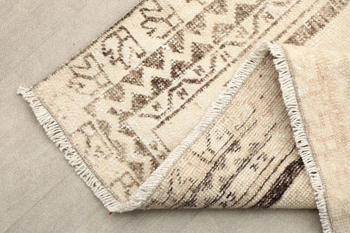 Corner of the rug folded back, showing the fringe and the hand-knotted construction