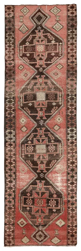 Full overhead view of a vintage rust and black geometric runner rug on a white background