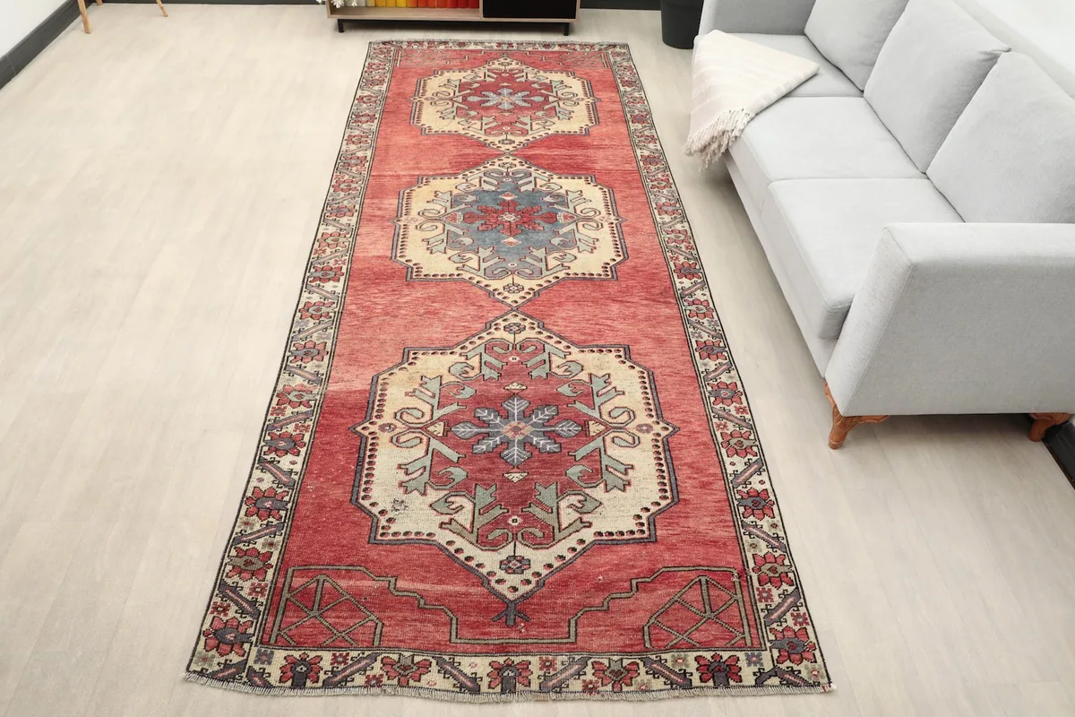 Vintage red runner rug displayed in a room setting, showing its long dimensions next to a light gray sofa.