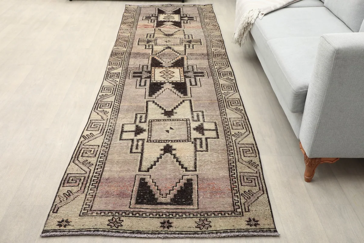 Vintage Anatolian runner rug shown in a room setting next to a light gray sofa, highlighting its length.