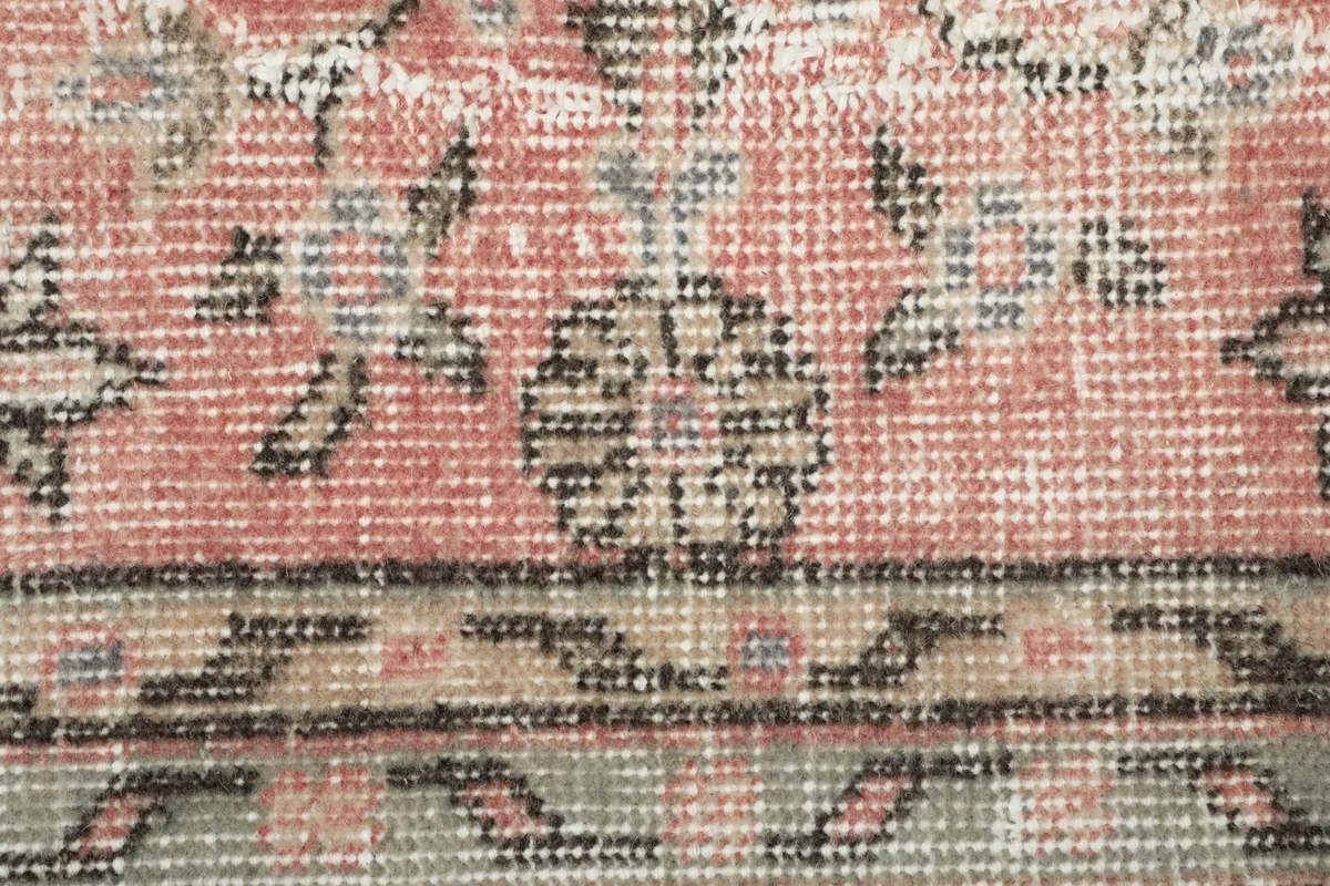 Extreme close-up of the rug's low pile, showing the hand-knotted wool texture and faded design details.
