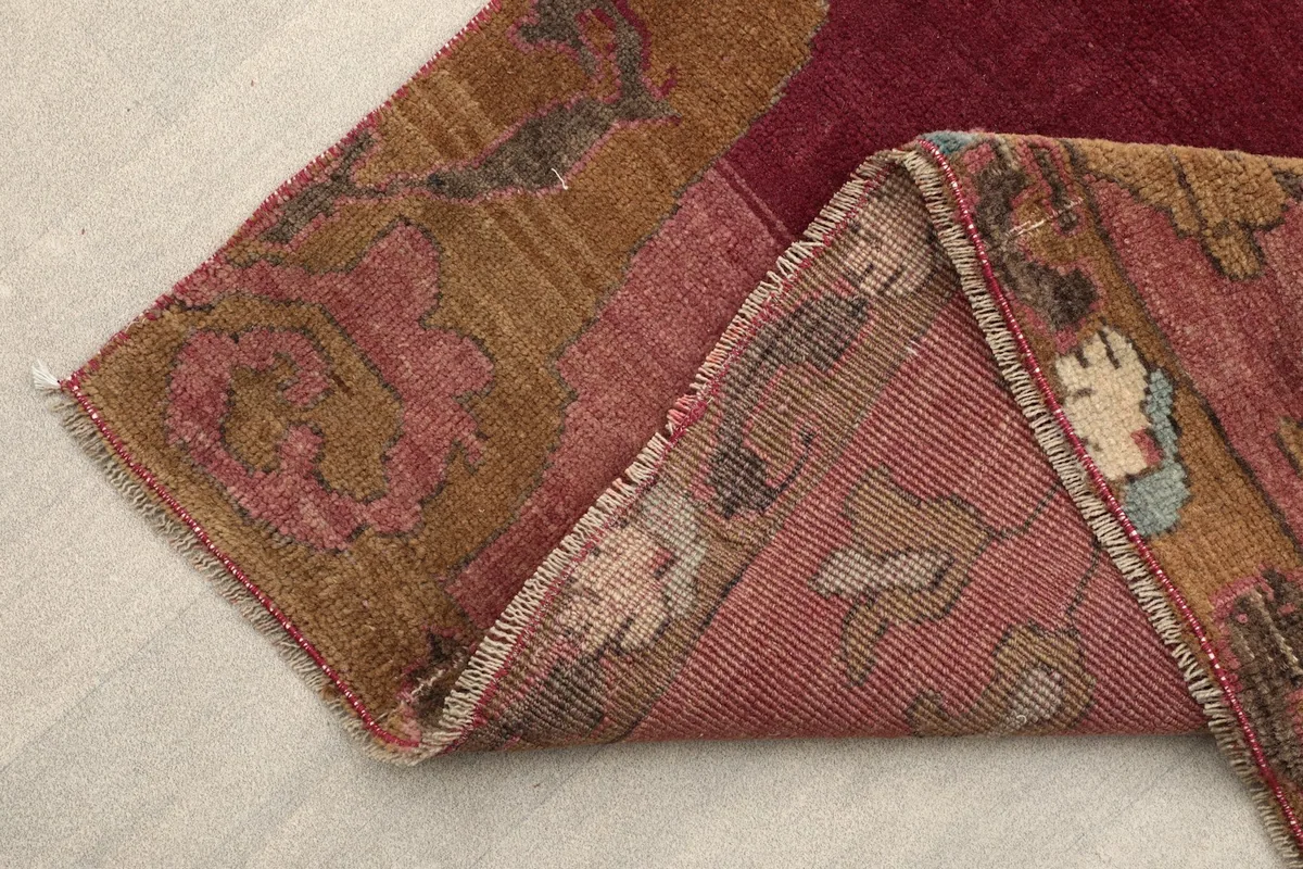 Folded corner of the rose rug, revealing the wool pile and cotton foundation.