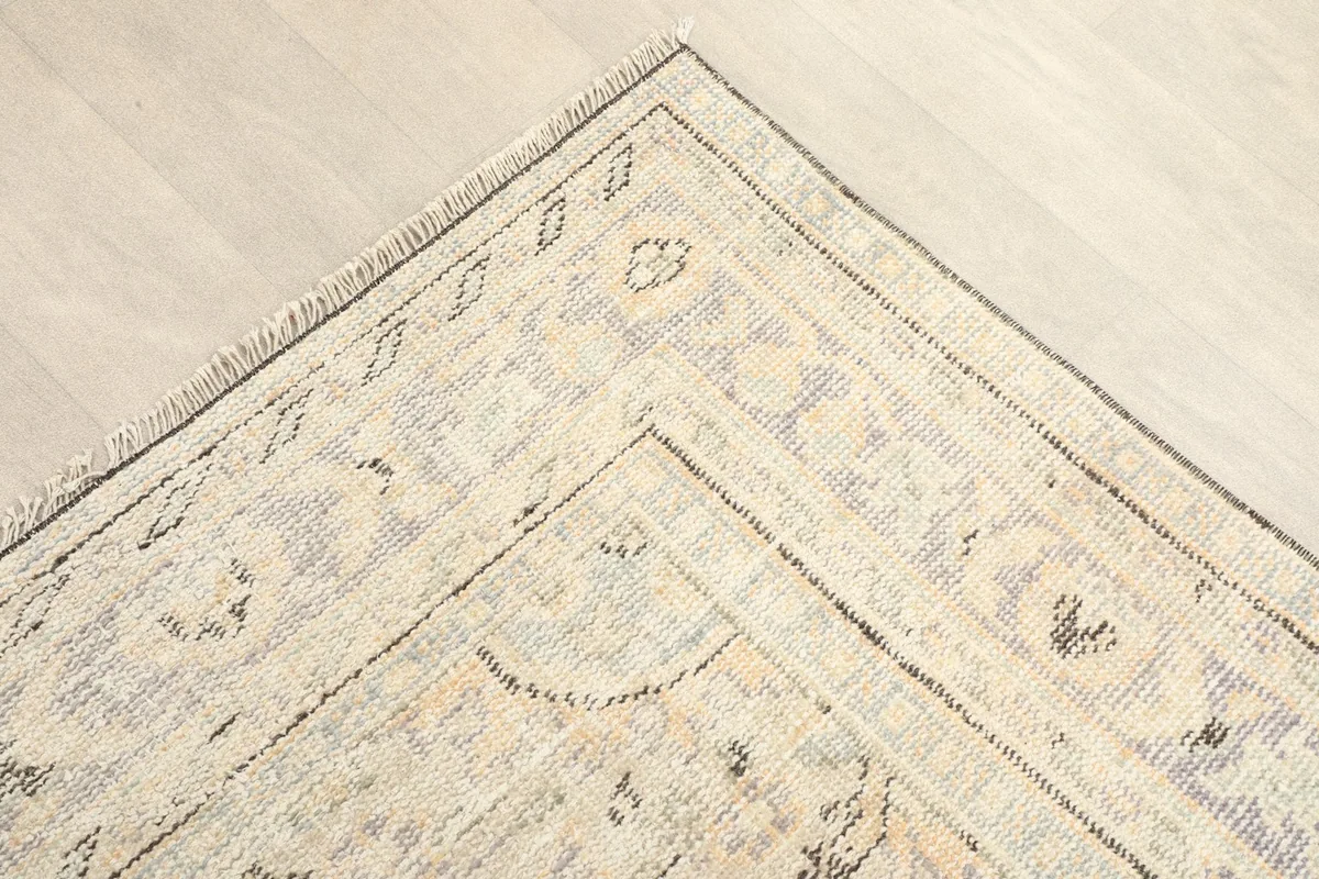 Corner detail showing the geometric patterns and muted gray and tan colors in the rug's border