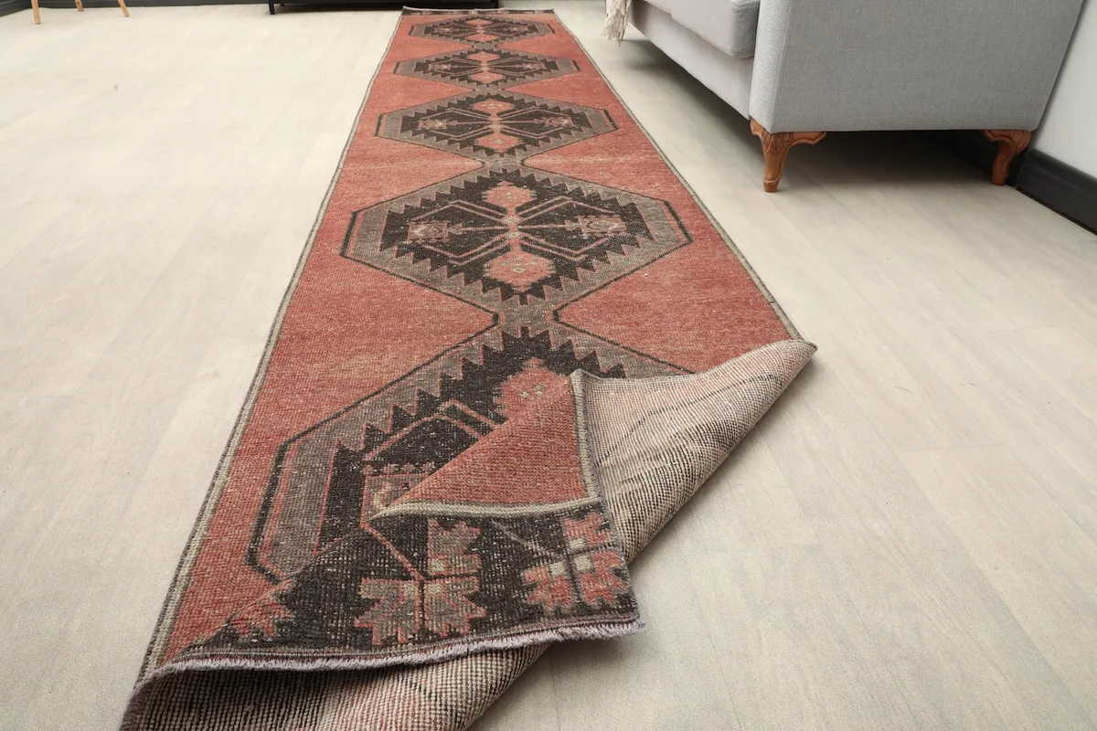 The rust geometric runner rug with one end folded back, showcasing its flexibility and construction in a room setting.