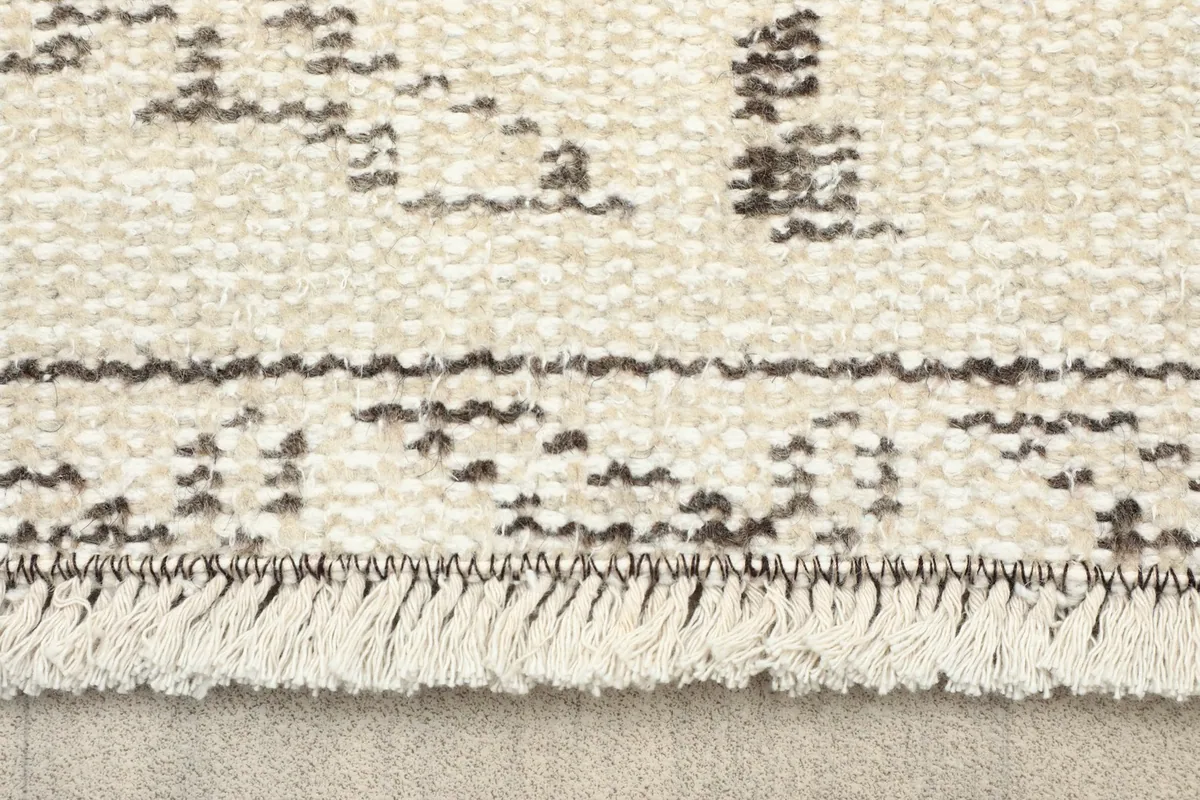 Close-up of the rug's fringe and a section of the faded gray and ivory design