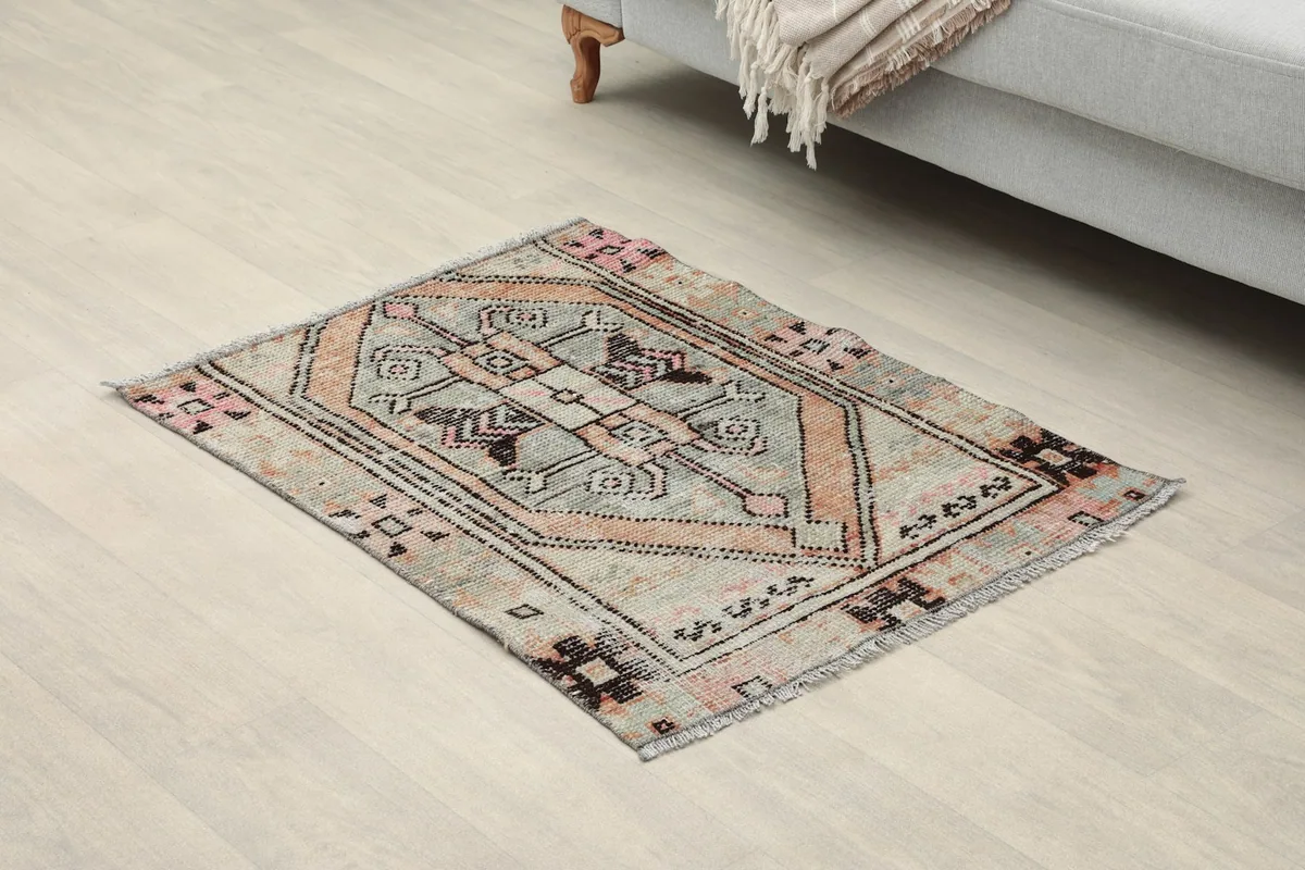 Angled view of the hand-knotted gray and rose rug on a light floor next to a sofa.
