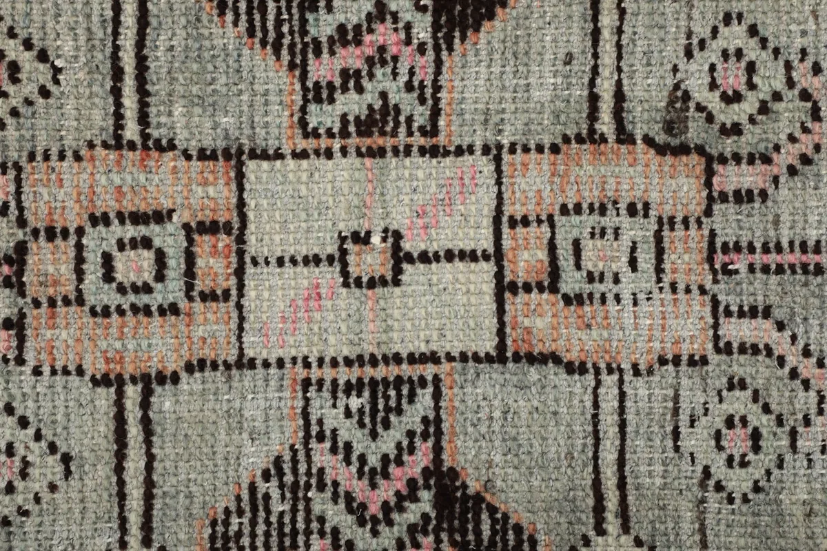Extreme close-up of the low wool pile, showing the texture and faded colors of the vintage rug.