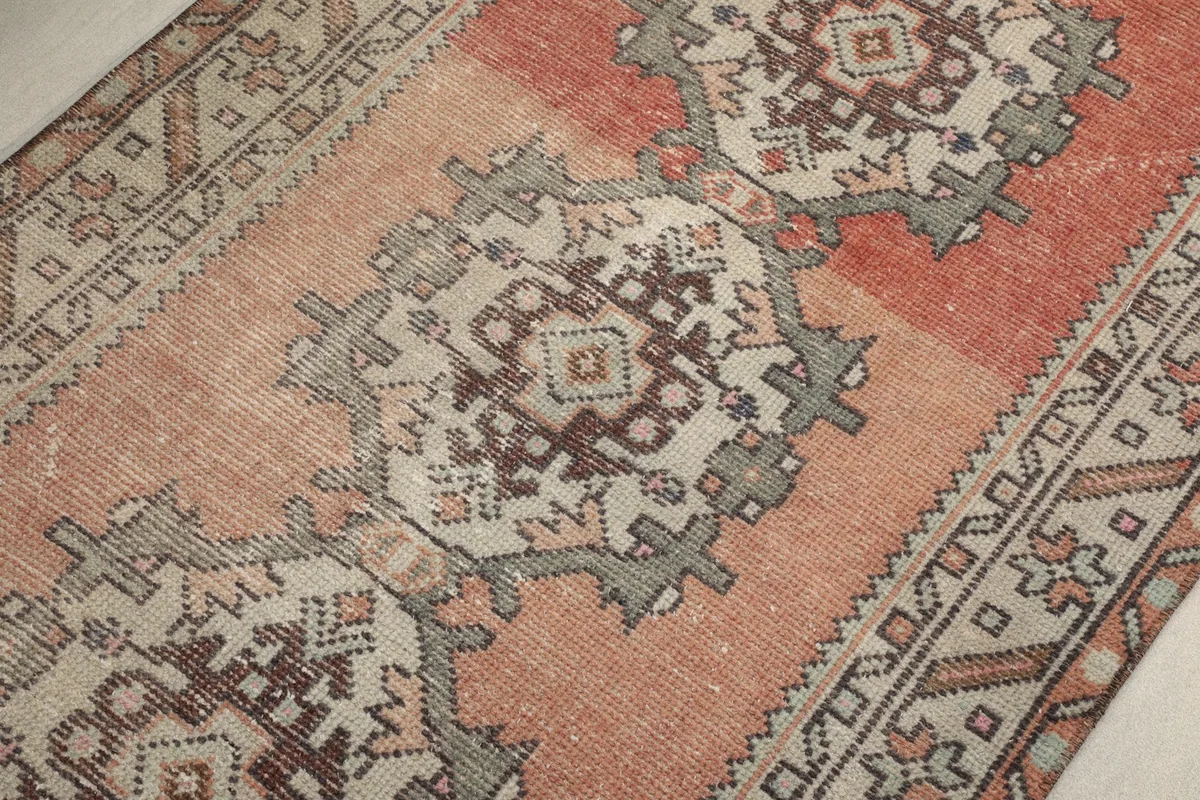 Detailed view of the faded rust and beige geometric motifs, highlighting the rug's vintage character.
