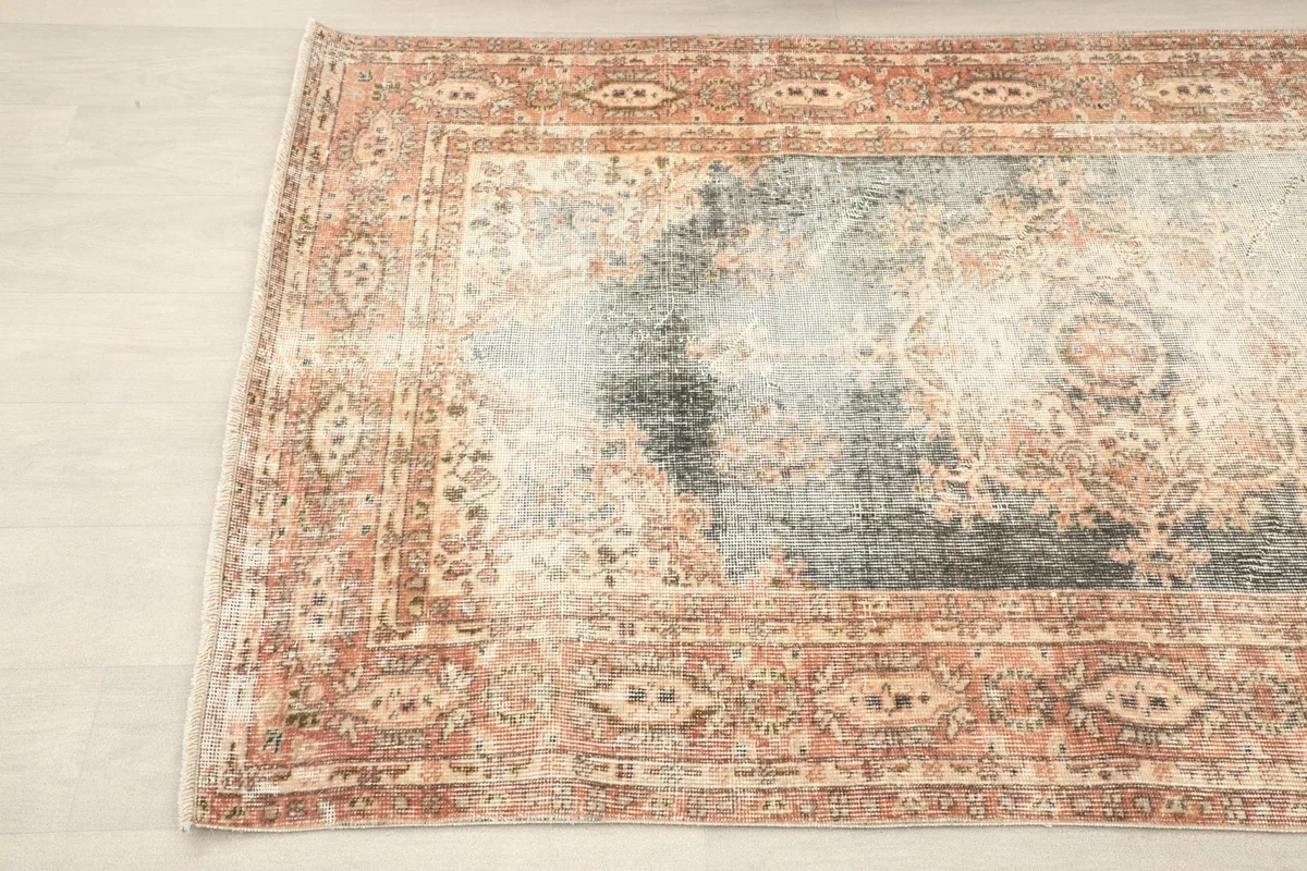 Corner angle of the rug, showcasing the faded colors and intricate details of the border.
