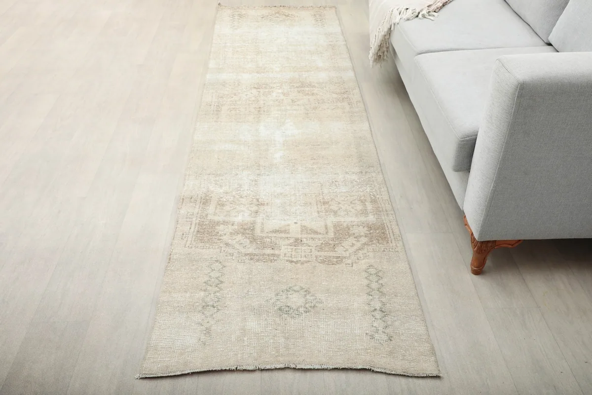 Vintage cream and tan runner rug placed in a living room next to a gray sofa, showing its length.