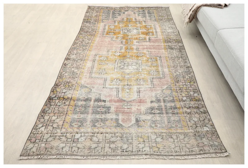 Full overhead view of the 4'1" x 8'0" vintage Anatolian rug with pink, gold, and gray colors on a white floor.